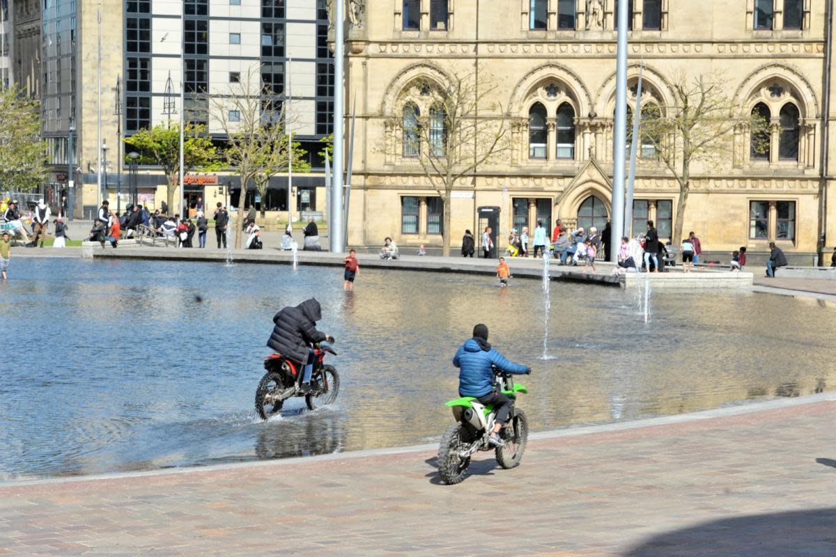 Two men ride through City Park in Bradford on dirt bikes as bemused children watch on <i>(Image: Telegraph & Argus)</i>