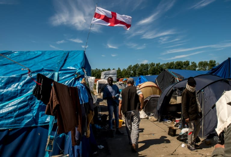 Migrants walk past a flag of England inside the "Jungle" camp for migrants and refugees in Calais on June 24, 2016