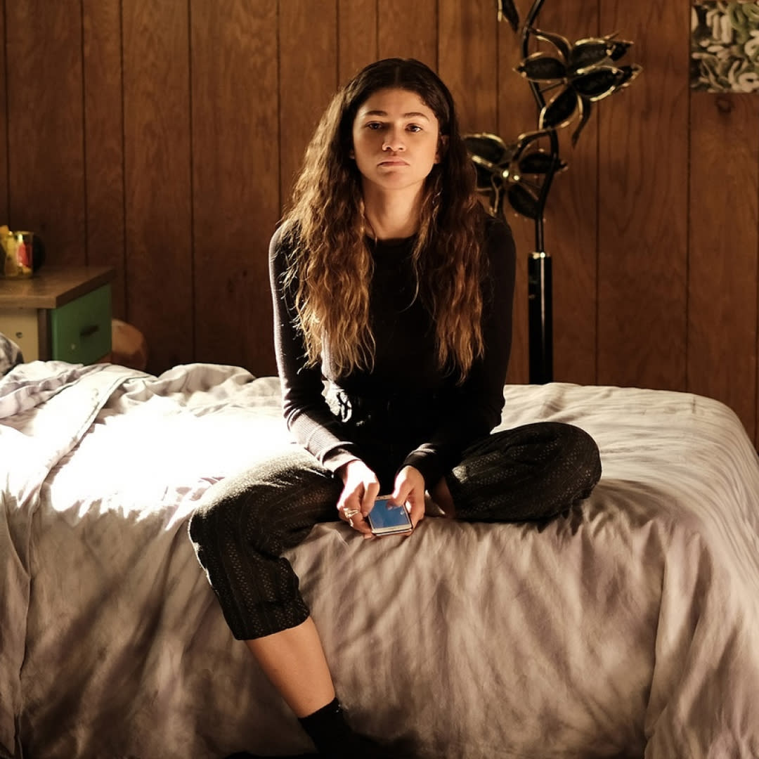  A woman (zendaya as rue) sits on a bed while holding a phone, in 'euphoria' season 2. 