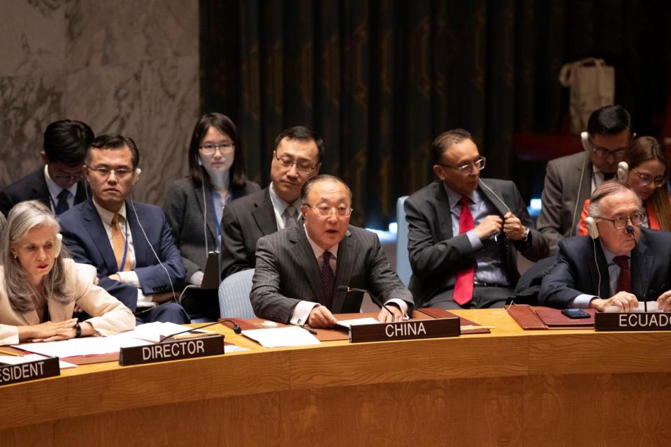 A man in dark gray suit and tie, sitting behind a placard that says China, is flanked by other seated people