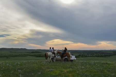 Members of the extended Lookinghorse family on three horses and in a car gather on a hilltop at dusk on the Cheyenne River Reservation in Green Grass, South Dakota, U.S., May 30, 2018. REUTERS/Stephanie Keith