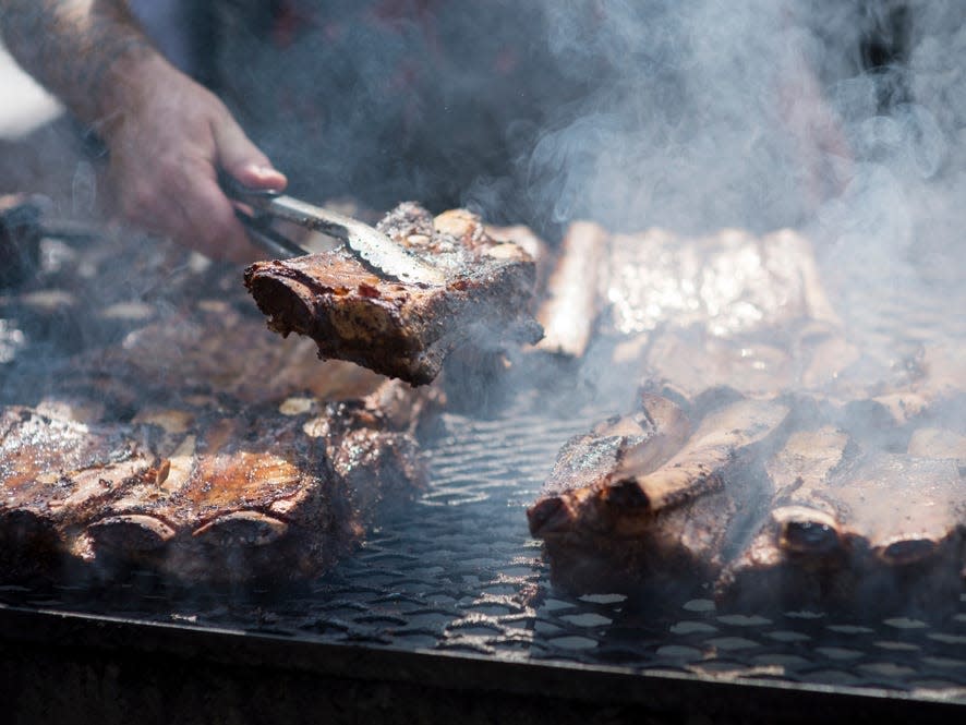 a person flipping barbecue ribs on a grill with smoke coming off it