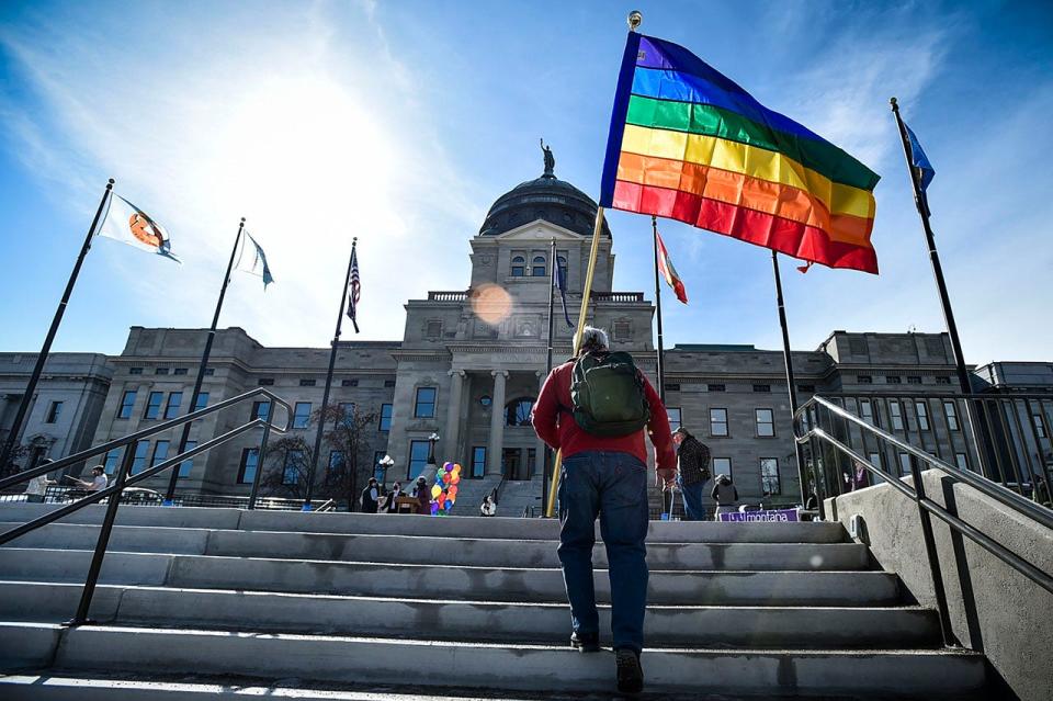 man carries rainbow flag up stairs outside Kansas state capitol