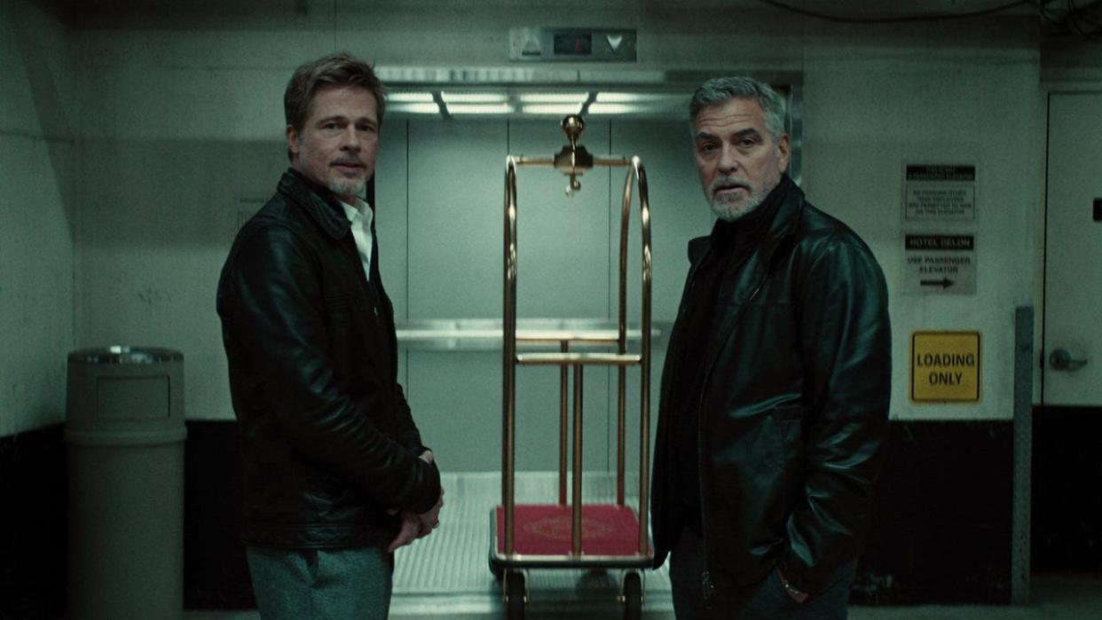 Brad Pitt and George Clooney standing in a lobby in leather jackets