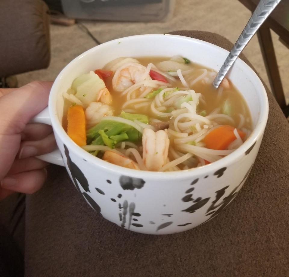 A person holding a bowl of shrimp and vegetable soup, with a storage container in the background