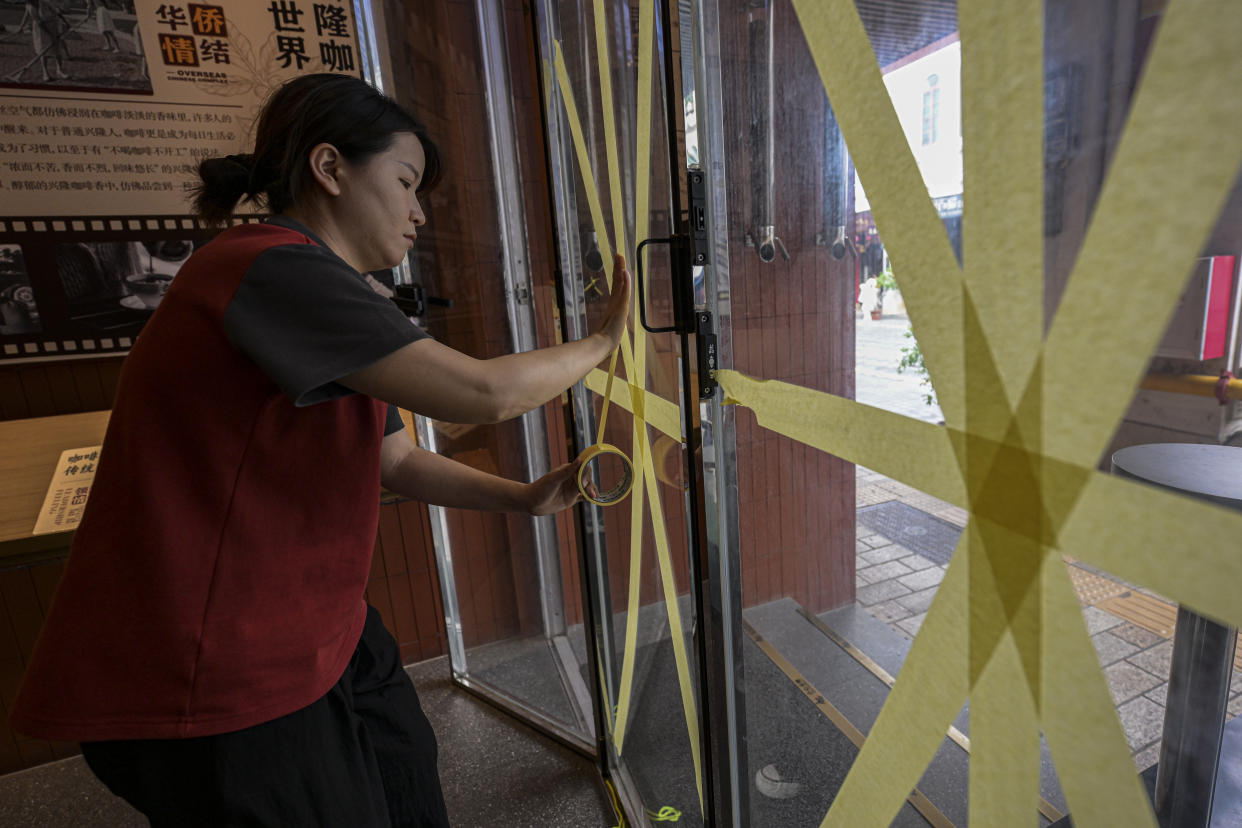 In this image released by Xinhua News Agency, a worker reinforces a glass window with tape at a cafe after the State Flood Control and Drought Relief Headquarters raised its emergency response for flood and typhoon prevention for Typhoon Yagi, Thursday, Sept. 5, 2024, in Haikou, south China's Hainan Province. (Pu Xiaoxu/Xinhua via AP)