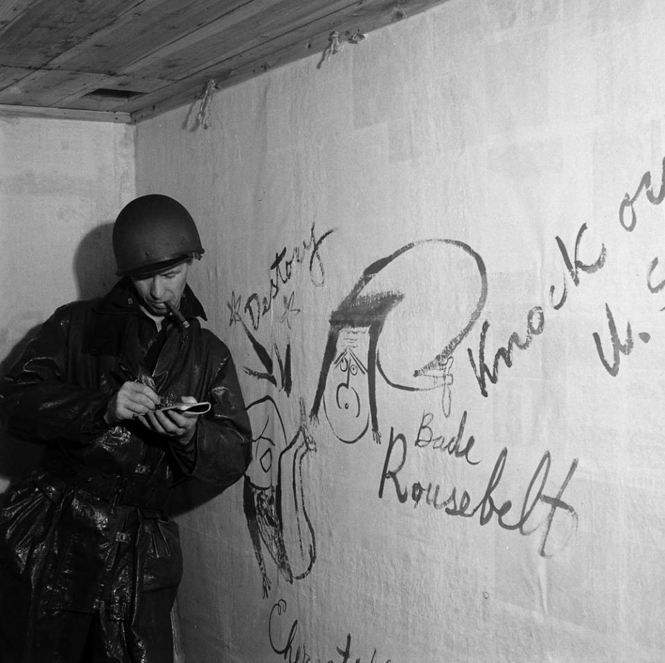 An American soldier leans against a wall in the captured Japanese headquarters on Kiska Island, beside graffiti caricatures of FDR and Churchill (left), 1943.