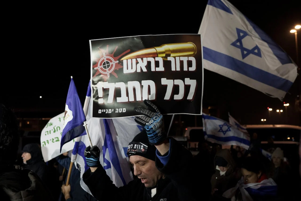 A man holds up a sign that says in Hebrew 