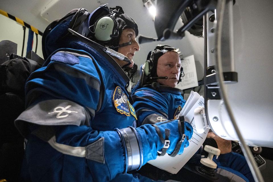 Two astronauts dressed in blue spacesuits inside a spaceship holding papers looking at the control panel