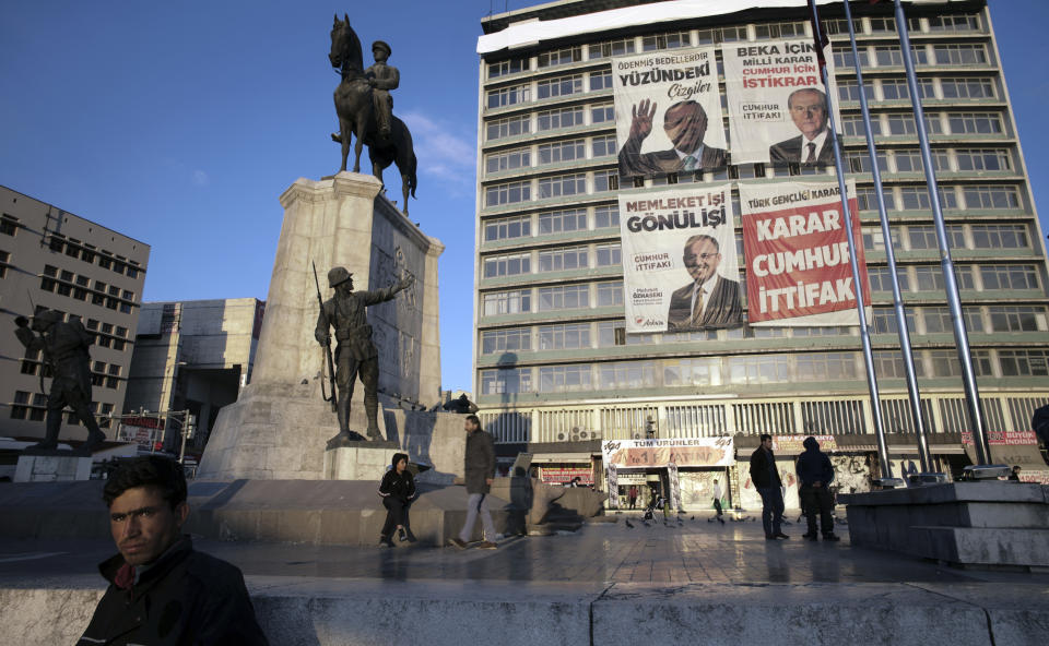 An unemployed man stands next to a statue depicting Turkey's War of Independence in old part of Turkish capital, Ankara, Turkey, Friday, March 29, 2019. A poster with images of Turkey's President Recep Tayyip Erdogan, top left, Devlet Bahceli, leader of the opposition Nationalist Movement Party, MHP, top right, and Mehmet Ozhaseki, the mayoral candidate for Ankara of Erdogan's ruling Justice and Development Party, AKP, and MHP is in the background, ahead of local elections scheduled for March 31, 2019. (AP Photo/Burhan Ozbilici)