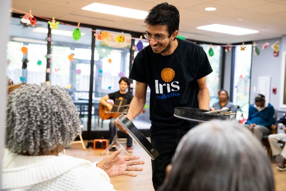 Pedro Maia, an artist fellow with the Iris Collective, hands a drum to a senior at Dorothy’s Place, a daycare center for adults with Alzheimer’s or dementia, as Otávio Kavakama, another fellow with Iris Collective, plays the guitar for the seniors to play along to at the facility in Memphis, Tenn., on Wednesday, April 10, 2024.