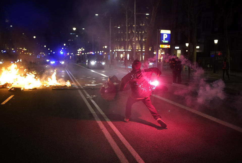 A demonstrator throws a flare at police during clashes after a protest condemning the arrest of rap singer Pablo Hasél in Barcelona, Spain, Tuesday, Feb. 16, 2021. Violent street protests have erupted in some Spanish cities after police arrested a rapper who resisted imprisonment and has portrayed his case as a fight for free speech. (AP Photo/Joan Mateu)