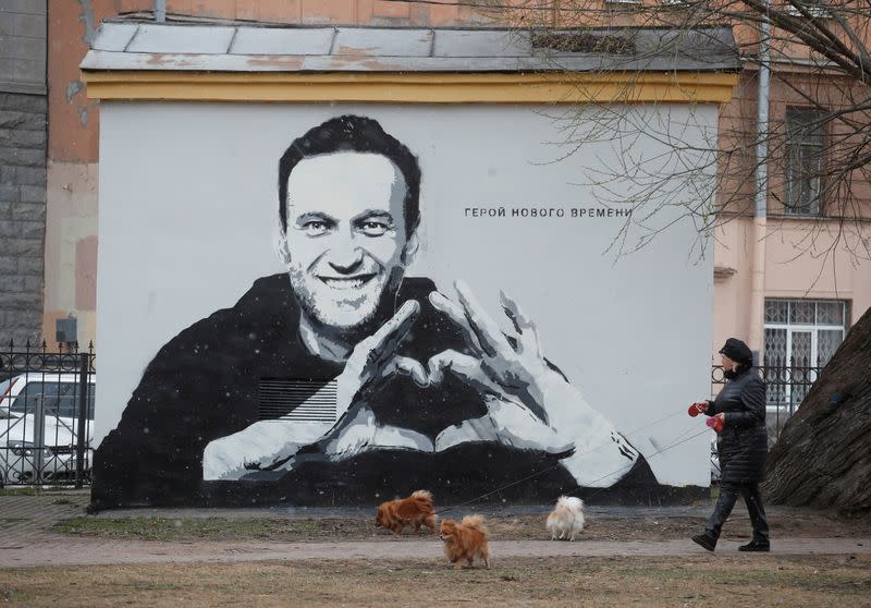 A woman walks her dogs in front of a graffiti depicting Alexei Navalny in Saint Petersburg