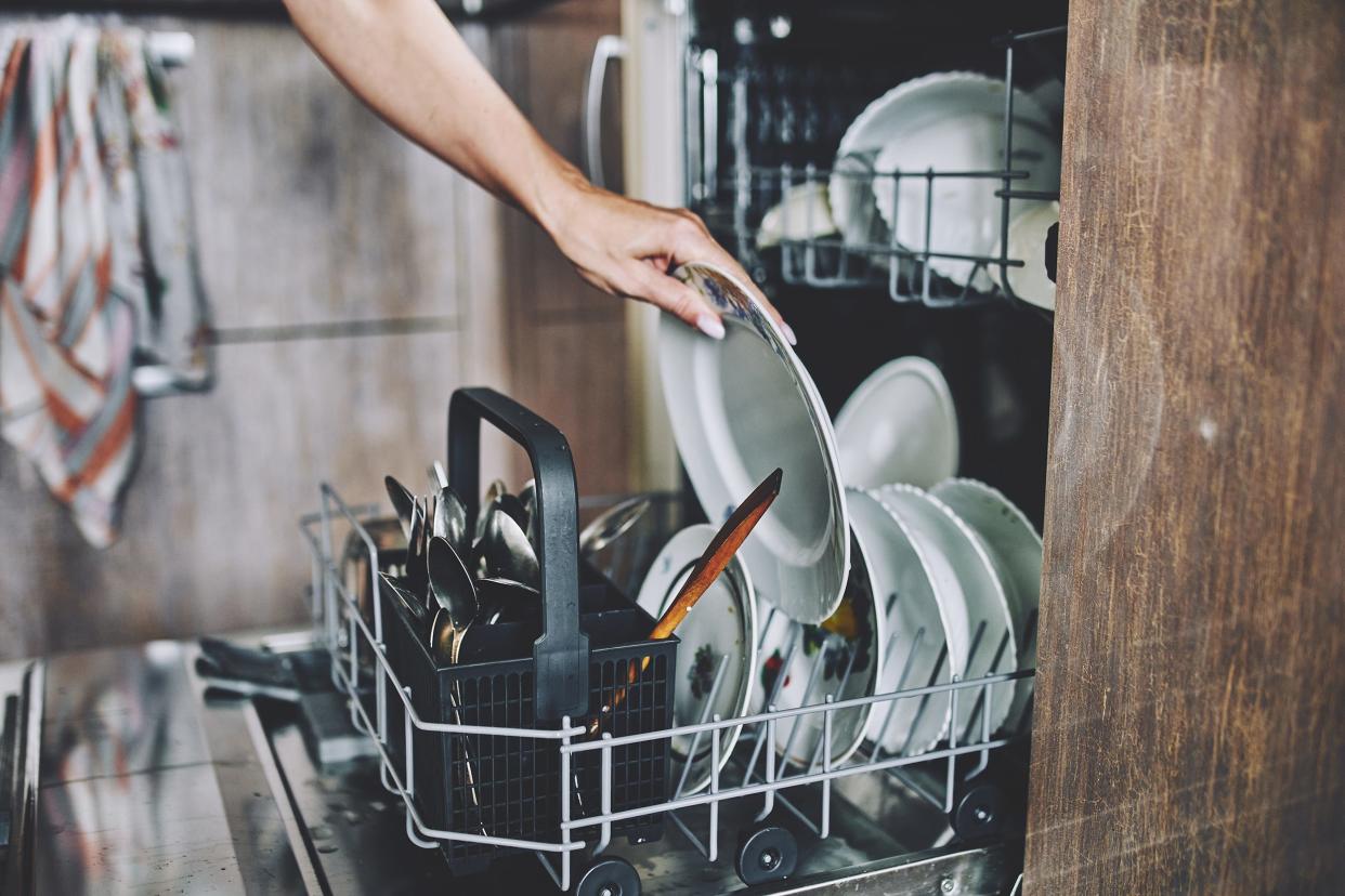 A hand loading a plate into a dishwasher.