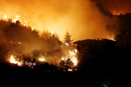 Flames rise next to a house as a wildfire burns near the village of Kalamos, north of Athens, Greece, August 13, 2017. REUTERS/Costas Baltas