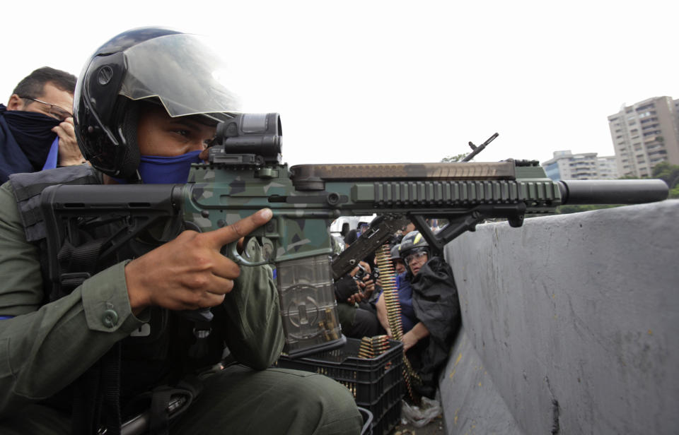 A rebel soldier who is part of a group rising up against the government of Venezuela's President Nicolas Maduro aims his weapon from an overpass at La Carlota military airbase where loyal troops are located, as members of the press and civilians take cover in Caracas, Venezuela, Tuesday, April 30, 2019. Venezuelan opposition leader Juan Guaidó and jailed opposition leader Leopoldo Lopez took to the streets with a small contingent of heavily armed troops early Tuesday in a bold and risky call for the military to rise up and oust Maduro. (AP Photo/Boris Vergara)