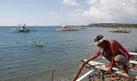 A fisherman repairs his boat overlooking fishing boats that fish in the disputed Scarborough Shoal in the South China Sea, at Masinloc, Zambales, in the Philippines April 22, 2015. REUTERS/Erik De Castro