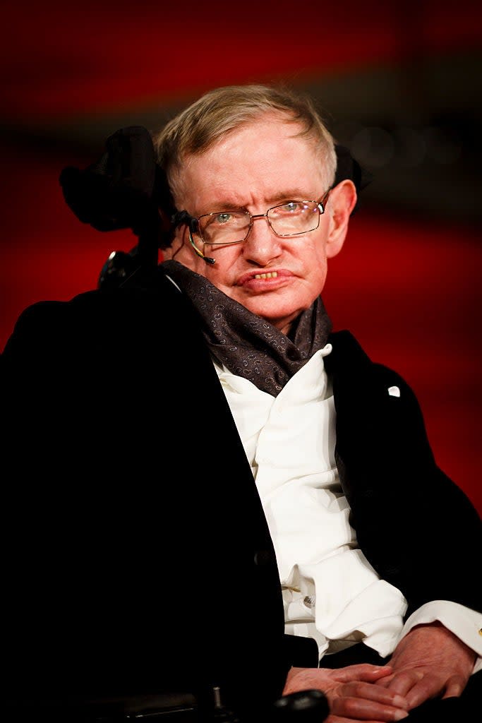 Stephen Hawking in a wheelchair wearing a suit with a dark scarf
