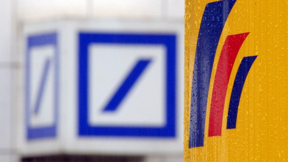 Das Logo einer Filiale der Deutschen Bank (l) und das Logo der auf der gegenüberliegenden Straßenseite befindlichen Postbank-Zentrale.