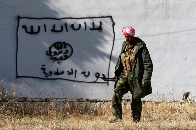 A Kurdish fighter walks by a wall bearing a drawing of the flag of the Islamic State group in the northern Iraqi town of Sinjar, on November 13, 2015