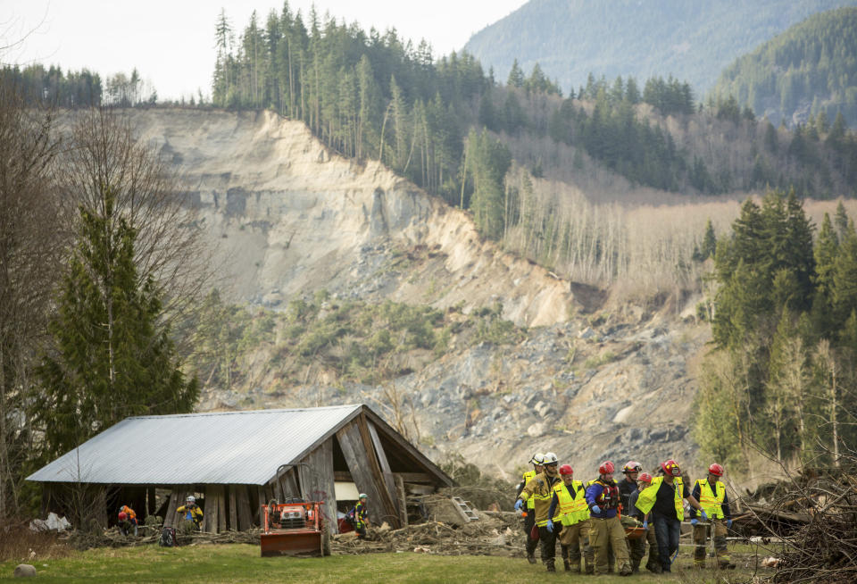 Rescue workers remove one of a number of bodies from the wreckage of homes destroyed by a mudslide near Oso, Wash., Monday, March 24, 2014. The search for survivors of Saturday's deadly mudslide grew Monday to include scores of people who were still unaccounted for as the death toll from the wall of trees, rocks and debris that swept through the rural community rose to at least 14. (AP Photo/seattlepi.com, Joshua Trujillo)