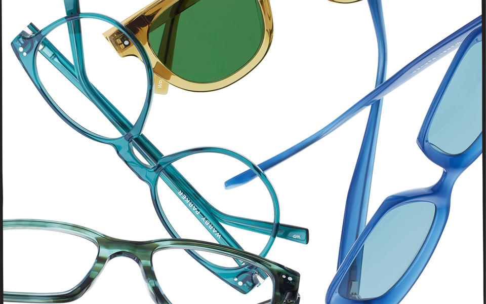 A pile of Warby Parker glasses in blue, green and yellow colors