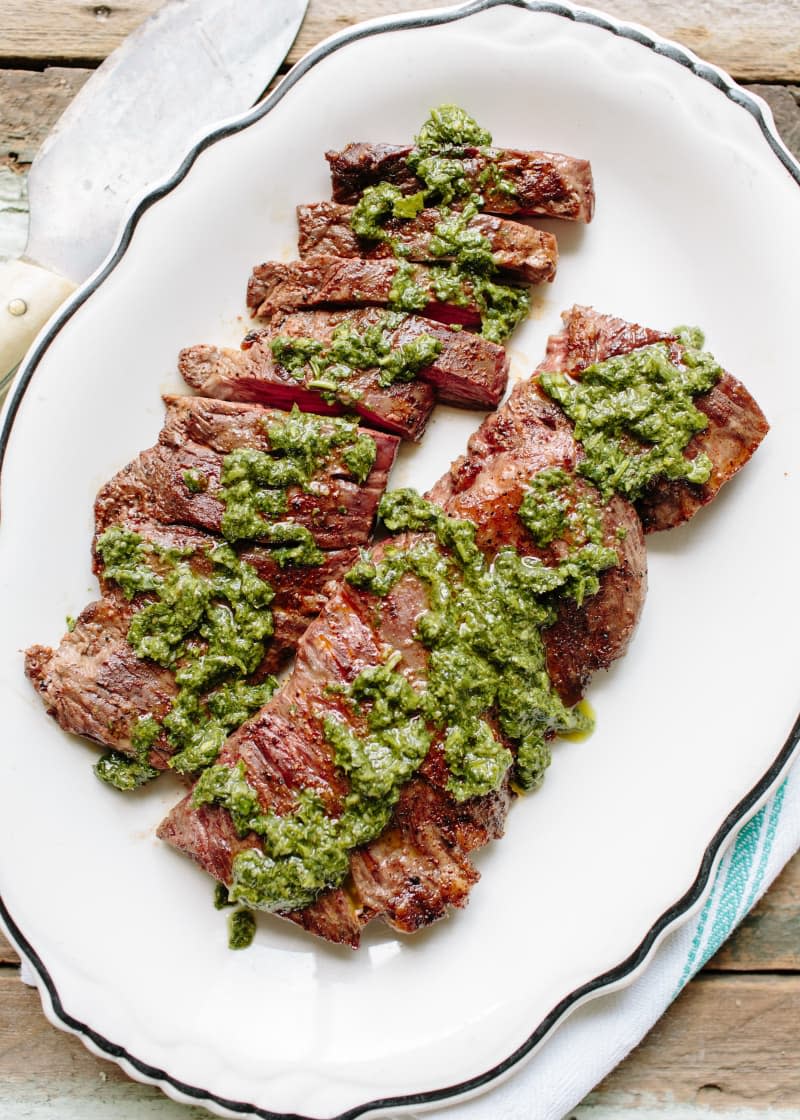 Two slabs of beef, topped with some pesto sauce, on a serving platter