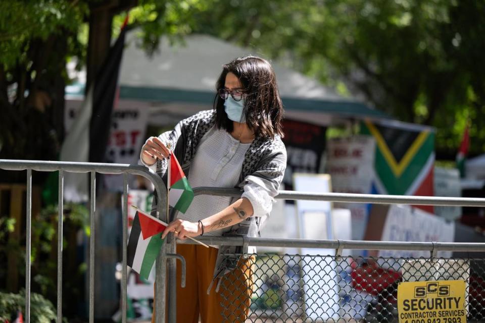 A pro-Palestinian activist inserts small Palestinian flags Wednesday into fence openings outside of the tented area the demonstrators took over three days ago at Sacramento State to protest the war in Gaza. Protesters are asking the university to divest in Israel.