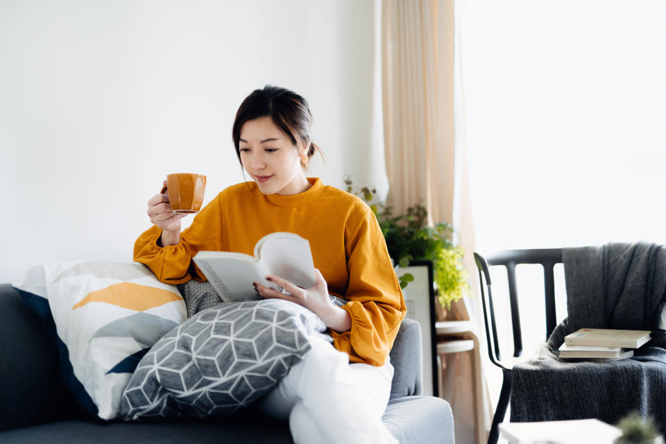 Beautiful young Asian woman reading a book while drinking a cup of coffee. Enjoying a quiet time and relaxing environment at cozy home