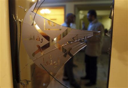 Members of the Muslim Brotherhood speak behind a door with shattered glass at the Muslim Brotherhood headquarters, which was attacked two days ago, in Cairo in this December 8, 2012 file photo. REUTERS/Amr Abdallah Dalsh/Files