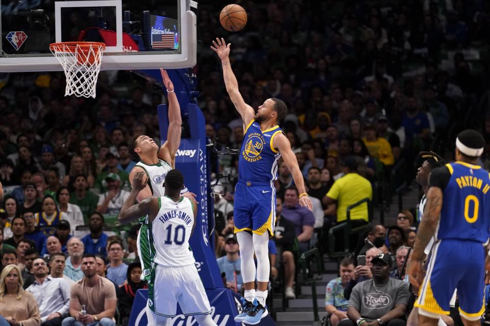 Dallas Mavericks' Dorian Finney-Smith (10) and Dwight Powell, left rear, defend against a shot by Golden State Warriors guard Stephen Curry (30) in the first half of an NBA basketball game in Dallas, Thursday, March, 3, 2022. (AP Photo/Tony Gutierrez)