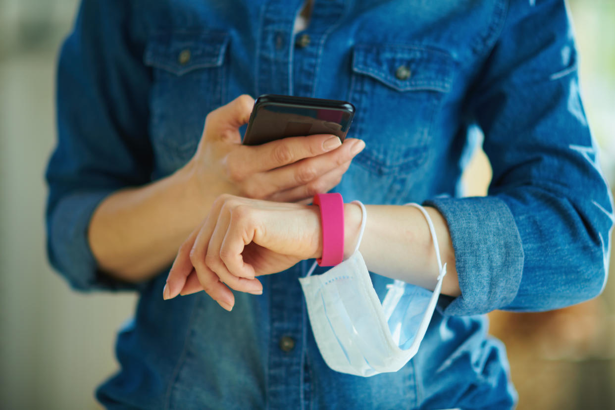 Closeup on modern middle age housewife with a smartphone and fitness tracker checking daily step stats in the house. Weight control on coronavirus quarantine concept