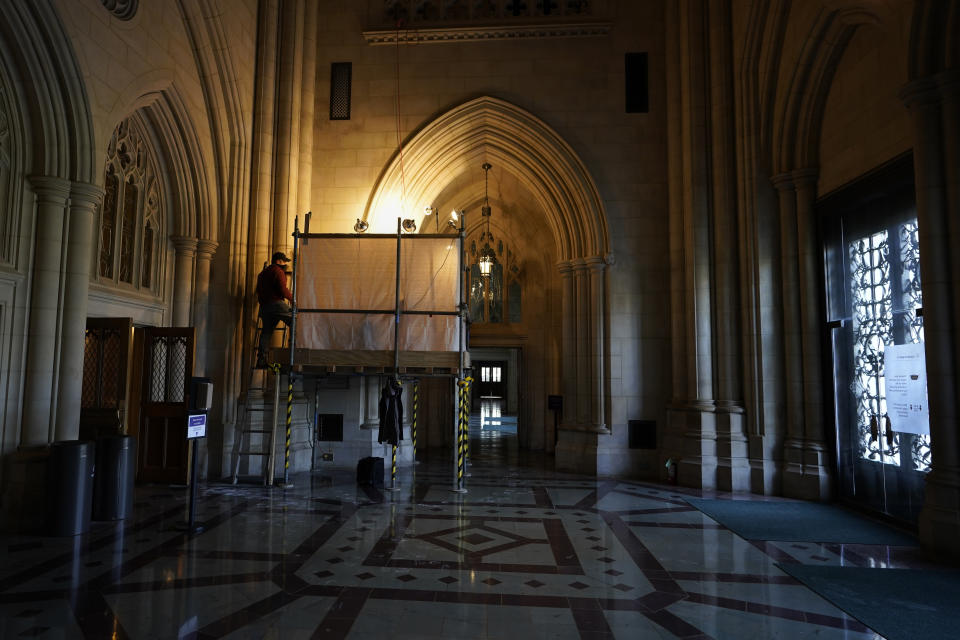 Stone carver Sean Callahan climbs a ladder to a scaffold to work on a sculpture of Holocaust survivor and Nobel Peace Prize winning author Elie Wiesel in the Human Rights Porch at the Washington National Cathedral, Friday, March 19, 2021. (AP Photo/Carolyn Kaster)