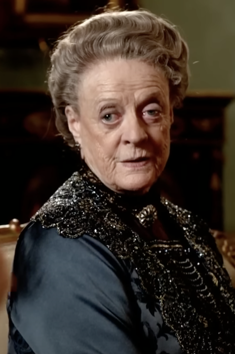 Maggie with styled hair in an embellished black dress, looking pensive