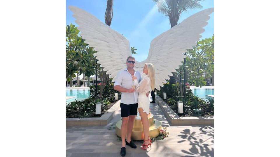 Amelia Spencer and Greg Mallett in front of angel wings by pool 