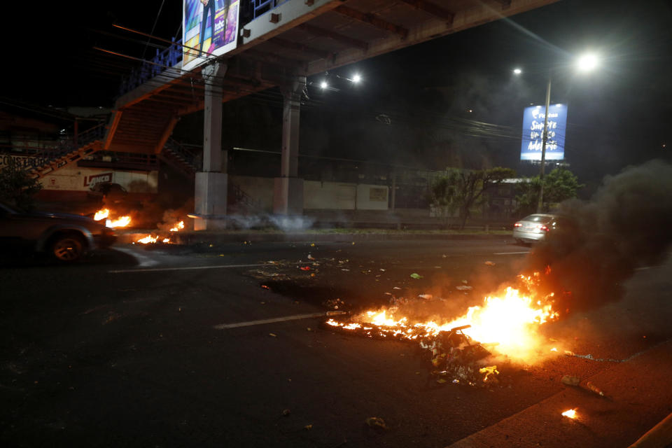 Cars speed past burning barricades during a night of rioting in Tegucigalpa, Honduras, late Thursday, June 20, 2019. Protesters blockaded highways, clashed with police as part of demonstrations against President Juan Orlando Hernández. (AP Photo/Elmer Martinez)