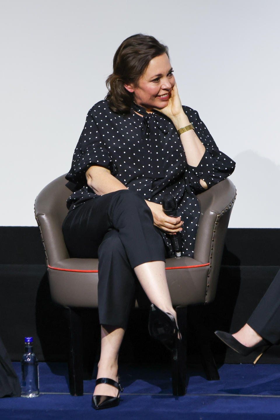 Olivia sits smiling in a chair with her hand under her chin at a Q&A