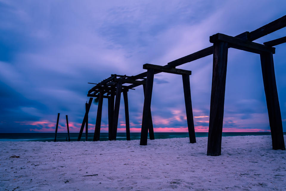 Remains of a pier leading out to the ocean at sunset