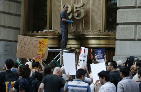 A man works on a scaffold as people protest against U.S. President Donald Trump's immigration policies in New York City, U.S., June 26, 2018. REUTERS/Brendan Mcdermid