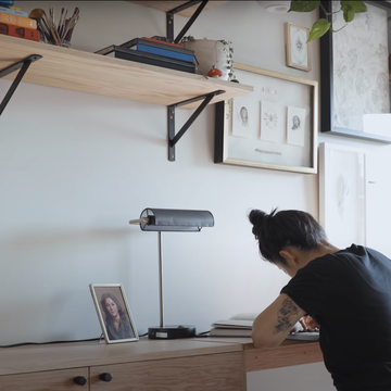 Person at their desk drawing next to a banker's lamp with a picture of a family member on their desk