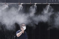 A man wearing a protective mask to help curb the spread of the new coronavirus cools down under a cooling mist spot at a street Wednesday, Aug. 12, 2020, in Tokyo. Hot weather Wednesday has set with temperatures rising up over 34 degrees Celsius (93.2 degrees Fahrenheit) in Tokyo, according to the Japan Meteorological Agency. (AP Photo/Eugene Hoshiko)