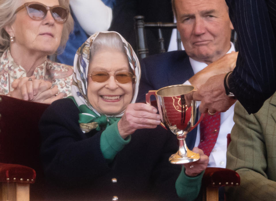 Queen Elizabeth II receives the winner's cup at The Royal Windsor Horse Show. She is wearing a headscarf. 