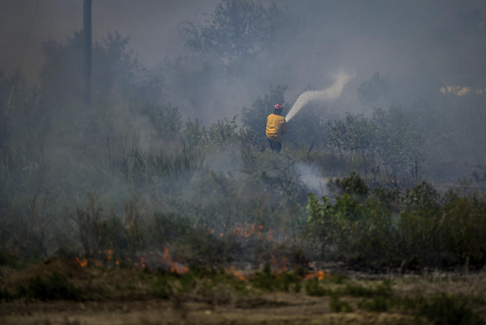 A firefighter directs water on a grass fire on an acreage behind a residential property in Kamloops, British Columbia, Monday, June 5, 2023. (Darryl Dyck/The Canadian Press via AP)