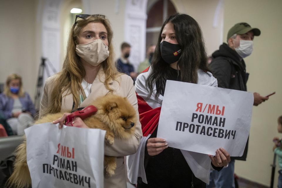 Women one of them wearing an old Belarusian national flag hold posters reading "I'm/we're Raman Pratasevich" as they wait to see passengers of the Ryanair plane with registration number SP-RSM, carrying opposition figure Raman Pratasevich which was traveling from Athens to Vilnius and was diverted to Minsk after a bomb threat, at the International Airport outside Vilnius, Lithuania, Sunday, May 23, 2021. The presidential press service said President Alexander Lukashenko personally ordered that a MiG-29 fighter jet accompany the Ryanair plane carrying opposition figure Raman Pratasevich and traveling from Athens, Greece, to Vilnius, Lithuania to the airport in the capital Minsk. (AP Photo/Mindaugas Kulbis)