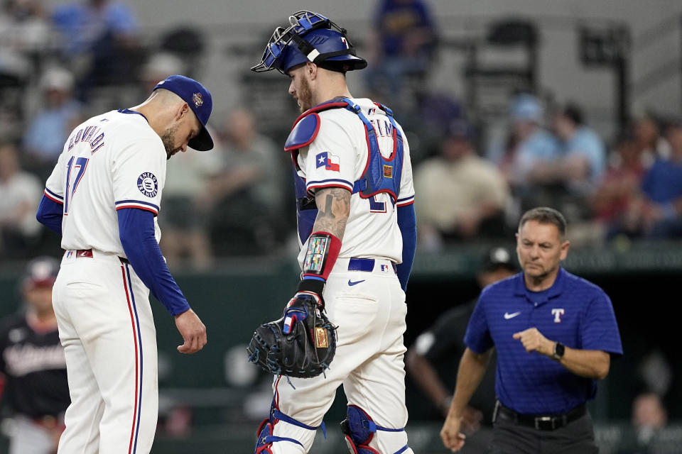 Texas Rangers starting pitcher Nathan Eovaldi, left, stands on the mound with catcher Jonah Heim as they wait on head athletic trainer Matt Lucero during the sixth inning of a baseball game against the Washington Nationals in Arlington, Texas, Thursday, May 2, 2024. Eovaldi left the game with an unknown injury. (AP Photo/Tony Gutierrez)