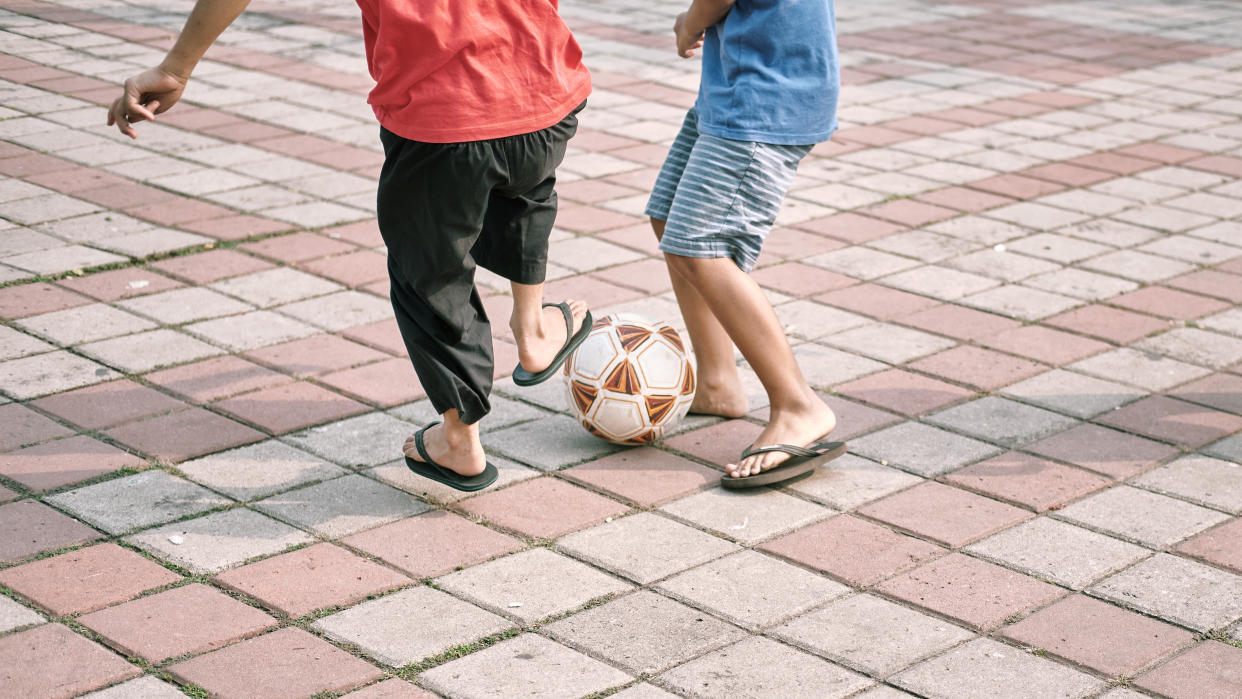 children's leg playing football with sandals on a paving stone