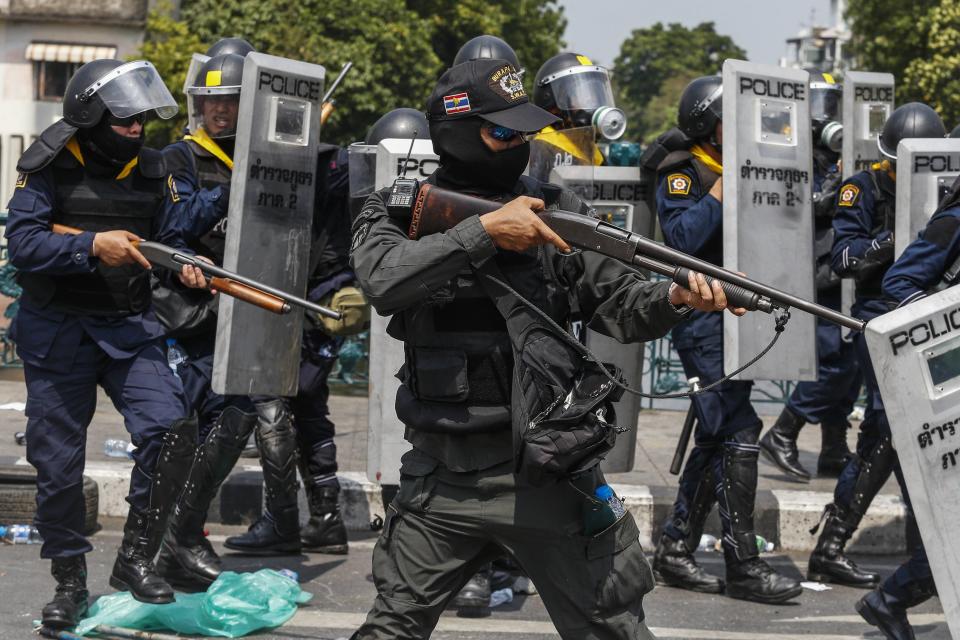 Thai police officers aim their weapons towards anti-government protesters after an explosion during clashes near the Government House in Bangkok