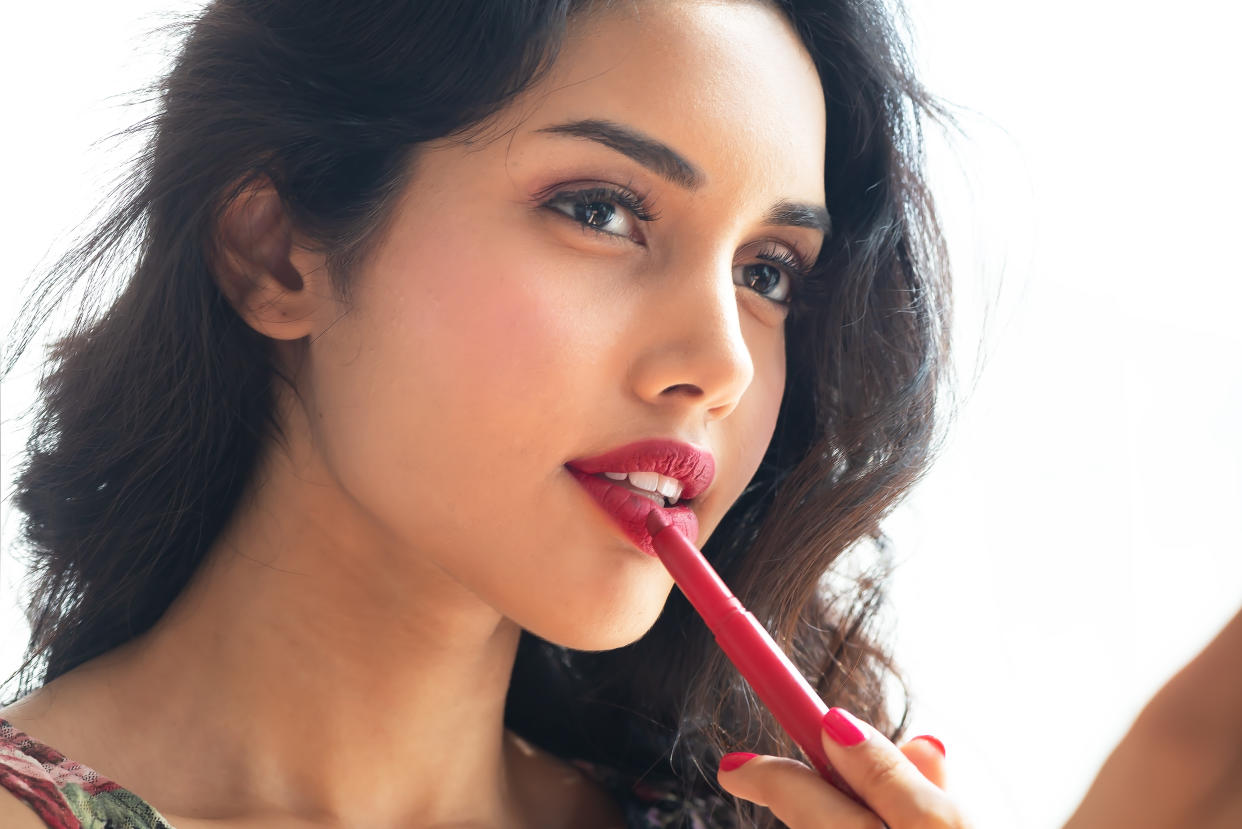 Beautiful young woman applying lipstick. (Photo: Getty)