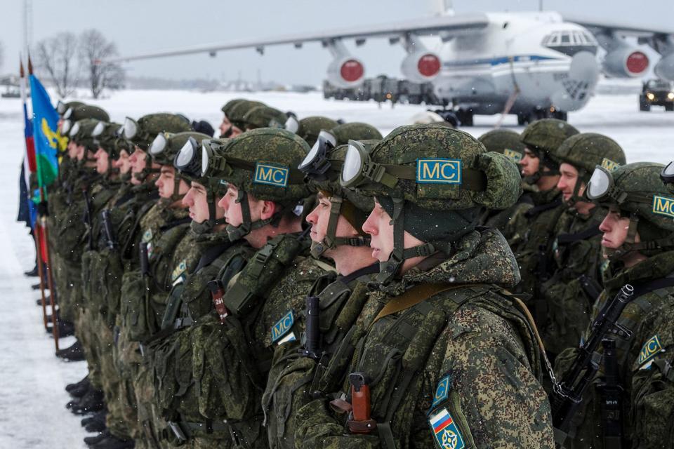 Soldiers stand in a row with snow on the ground and an aircraft behind them