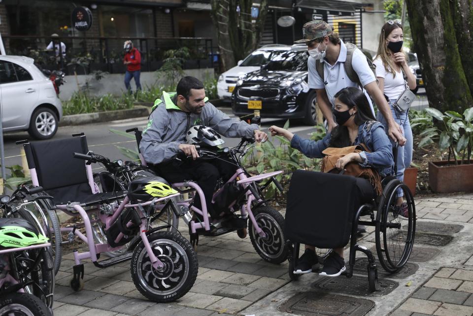 Martín Londoño (izq) saluda a una clienta que participará en un recorrido de los principales puntos turísticos de Medellín en sillas de ruedas eléctricas el 18 de noviembre del 2020. (AP Photo/Fernando Vergara)